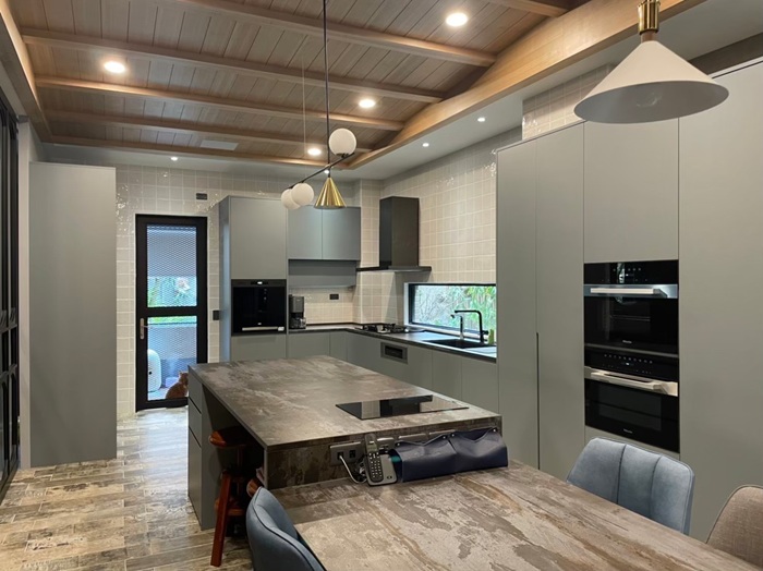 開放式廚房以灰色 EGGER 板材打造櫥櫃，搭配石紋中島與黑色電磁爐，線條俐落，搭配玻璃推門與室外光線，使整體空間明亮通透。