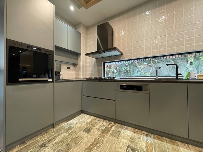 EGGER 板材打造的極簡灰色廚櫃，結合白色立體方格瓷磚與黑色家電，透過大面橫向窗戶引入自然綠景，營造舒適的烹飪氛圍。